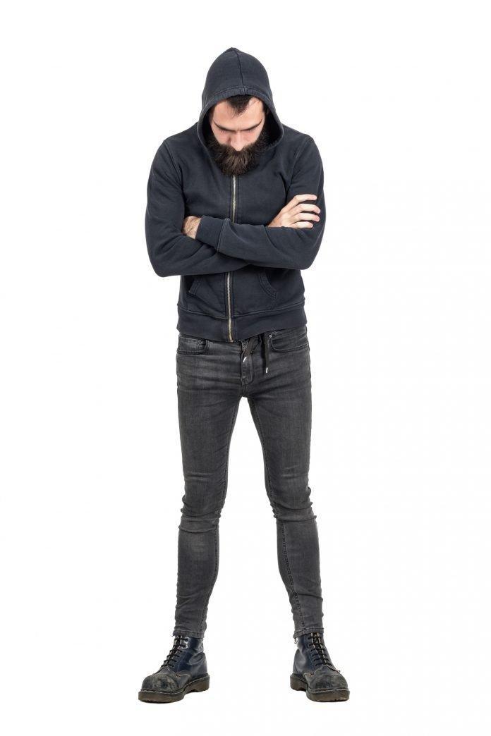 Tough punker in hooded sweatshirt with crossed arms looking down
