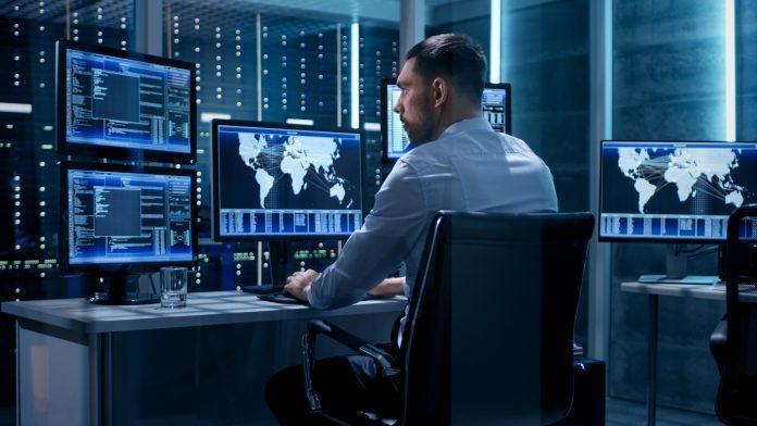 Technical Controller Working at His Workstation with Multiple Displays. Displays Show Various Technical Information. He's Alone in System Control Center. War Room